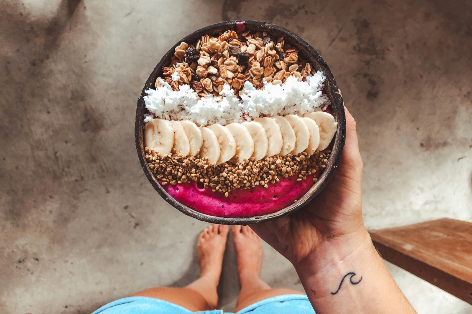 Pinke Smoothie-Bowl mit Granola, Kokosflocken und Bananenscheiben in einer Kokosschale