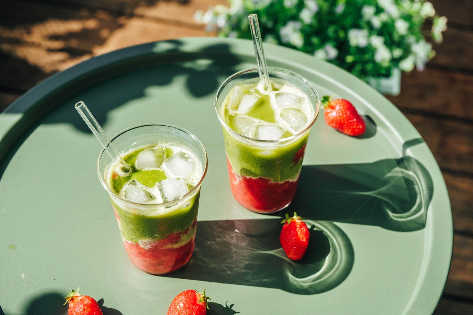 Zwei Strawberry Iced Matcha Lattes mit Erdbeerpüree, Eis und Glasstrohhalm