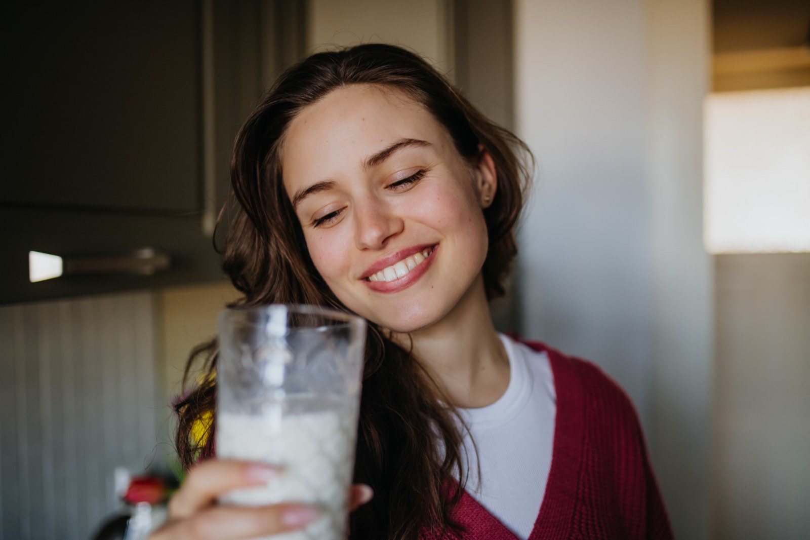 Lächelnde junge Frau hält in der Küche ein Glas Pflanzenmilch in der Hand