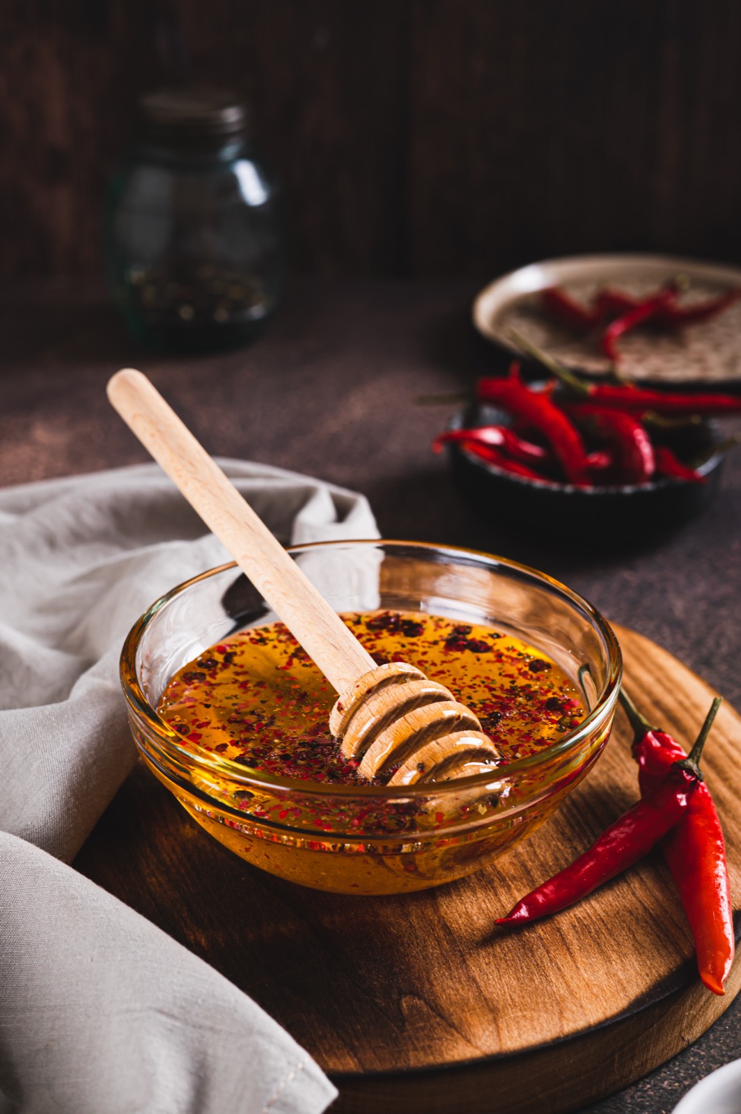 Honey with chili flakes in a glass bowl with a honey spoon, with fresh red chili peppers next to it