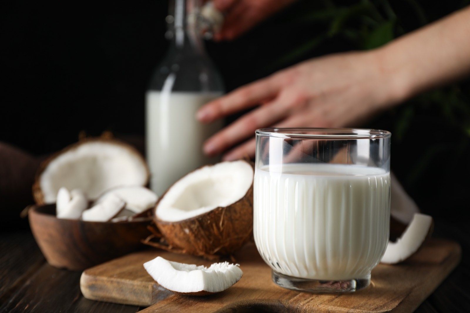 Coconut milk in a fluted glass, with cracked open coconuts on a wooden board in front of it