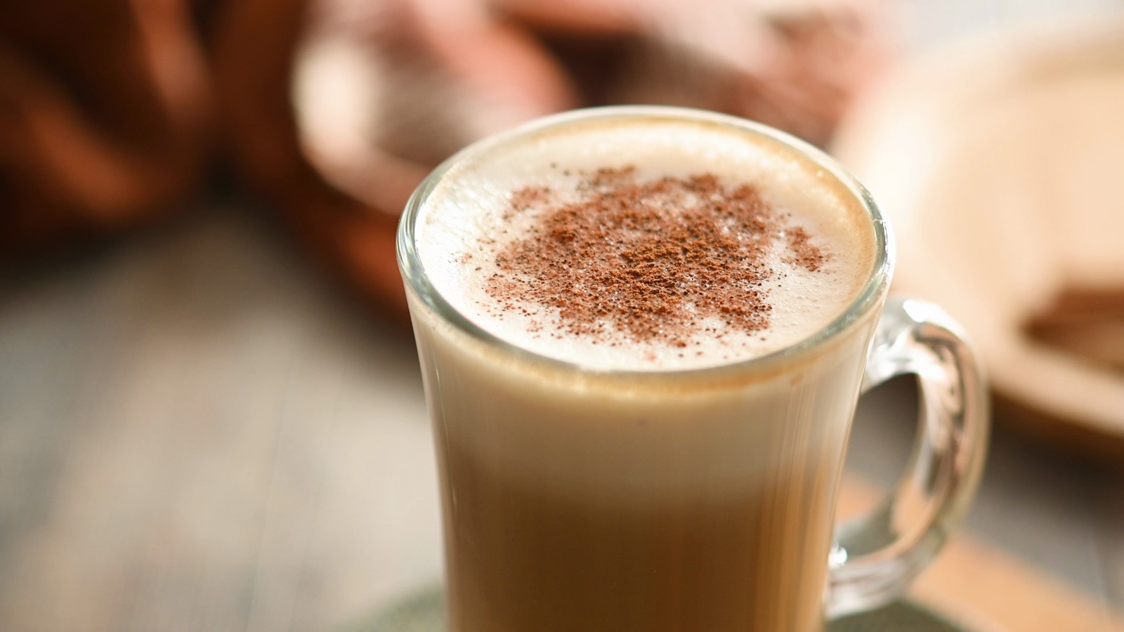 Latte with cinnamon sprinkled on top of the milk foam, served in a glass mug with a handle