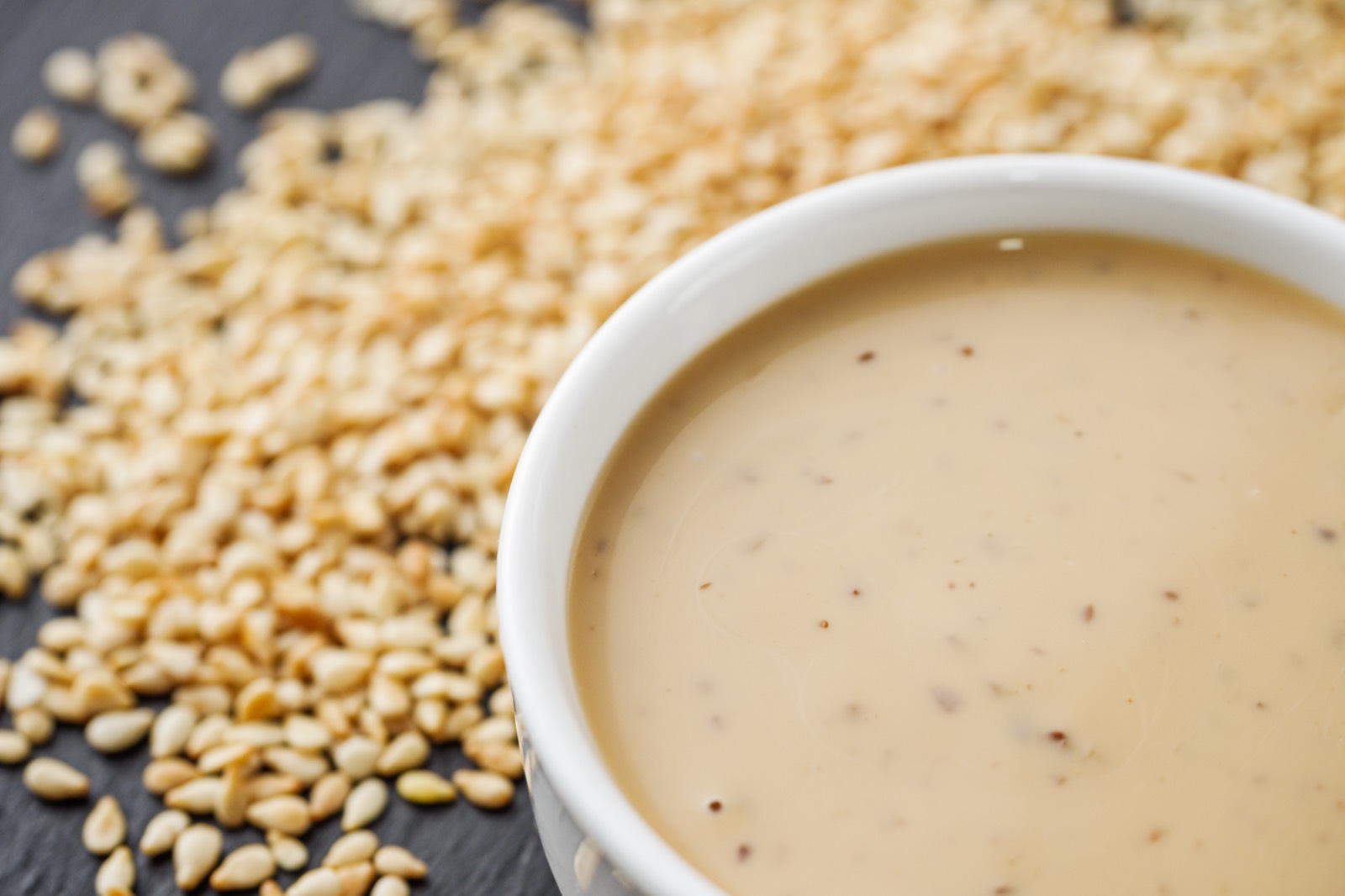 Creamy tahini made from sesame seeds in a white bowl, with roasted sesame seeds beside it